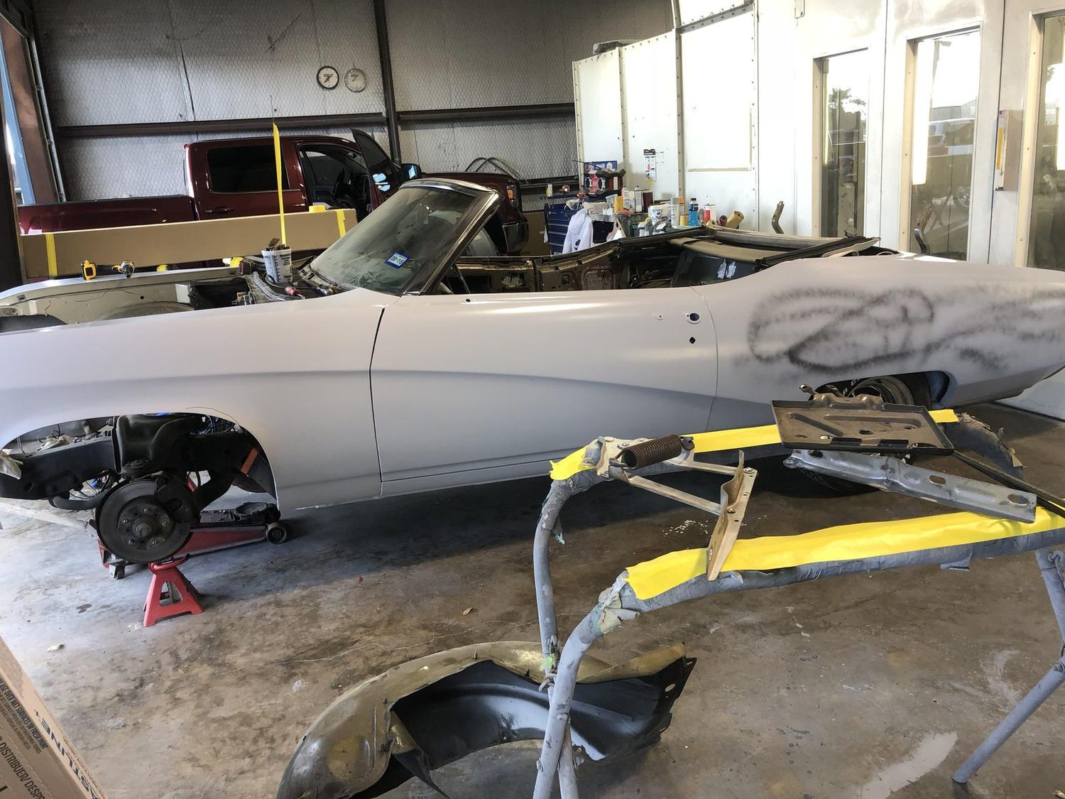 1969 Buick GS convertible torn down to primer on jack stands, bumper and wheels removed